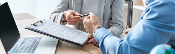 cropped view of travel agent giving contract and pen to client, panoramic shot