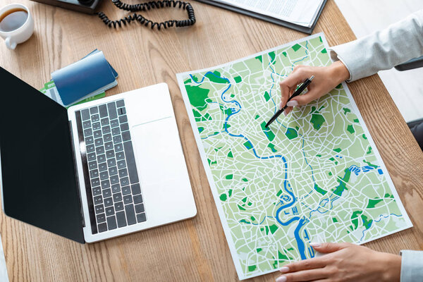 cropped view of travel agent pointing with pen at map on wooden desk