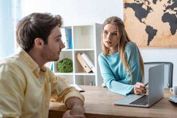 attractive travel agent looking at client while pointing at laptop screen