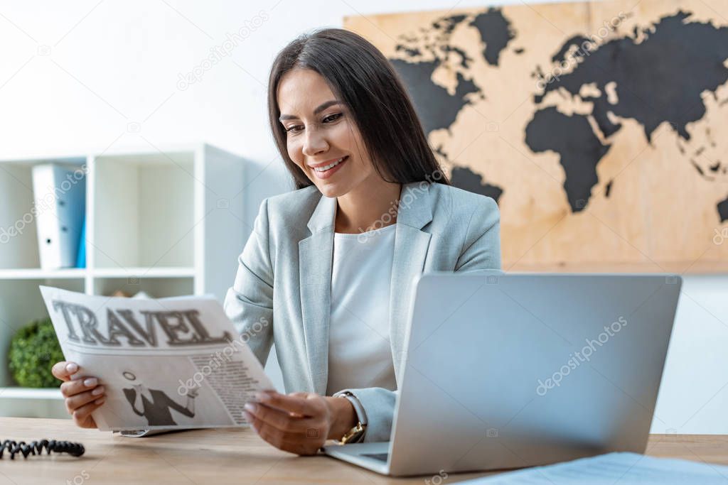 smiling travel agent reading travel newspaper at workplace