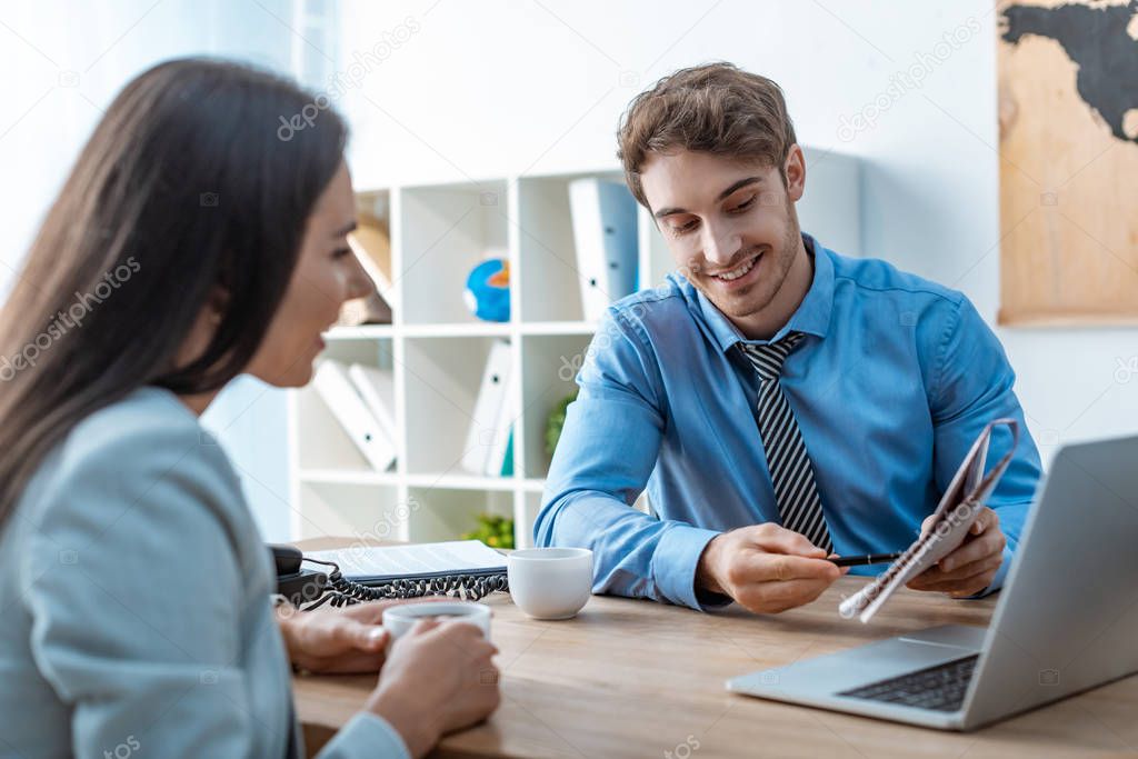 smiling travel agent pointing with pen at map while talking to client