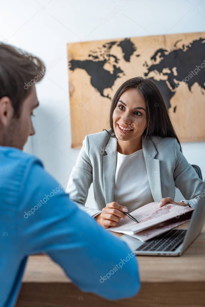 smiling travel agent pointing with pen at map while talking to client