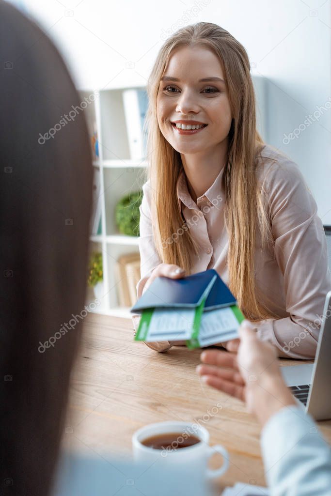 selective focus of smiling travel agent giving passports and air tickets to client