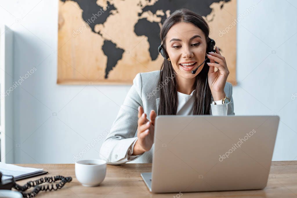 attractive travel agent in headset working near laptop