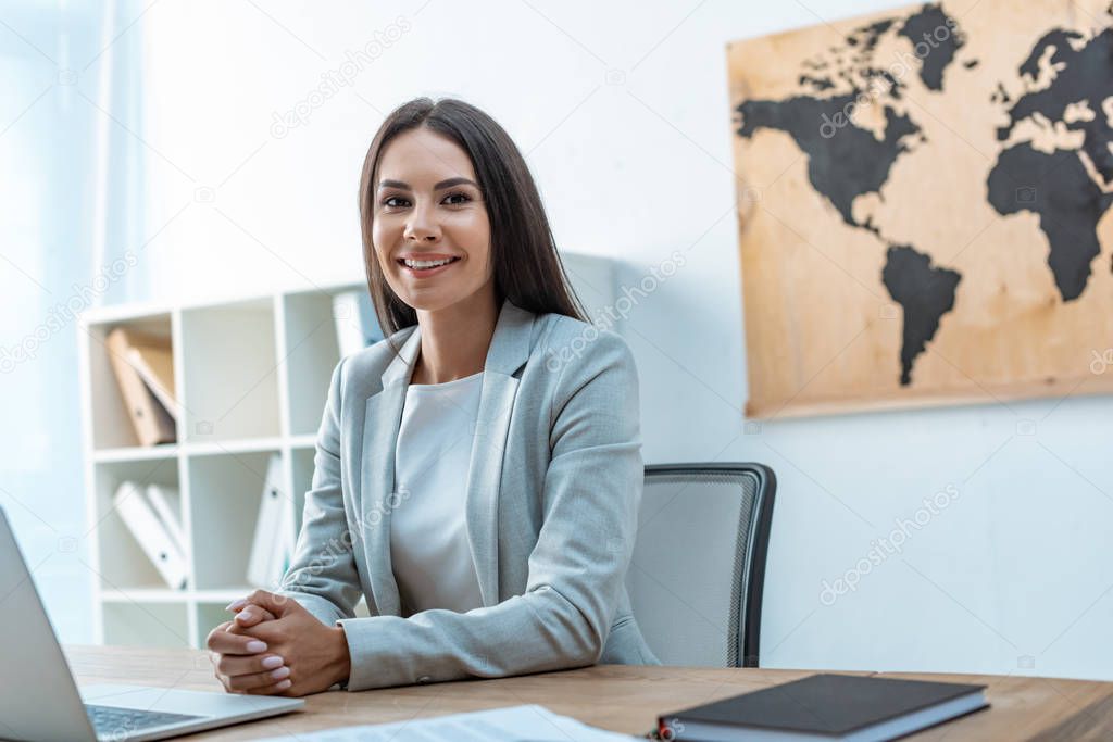 attractive travel agent looking at camera while sitting at workplace