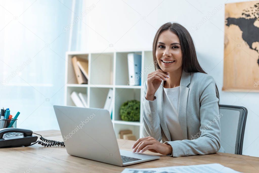 beautiful travel agent smiling at camera while sitting at workplace