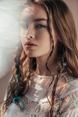 attractive ethnic girl with braids in hairstyle posing in white boho dress on grey with lens flares  clipart