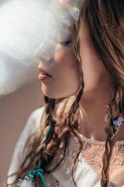 tender girl with closed eyes and braids in hairstyle posing in white boho dress on grey with lens flares  clipart