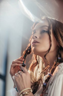 attractive thoughtful girl with braids in hairstyle posing in white boho dress on grey with lens flares  clipart