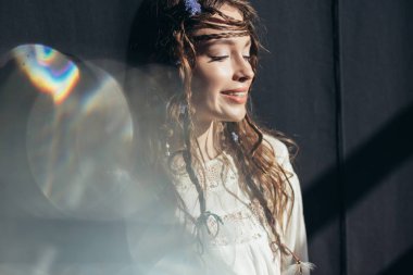 Saçları örülü mutlu bir kız. Beyaz boho elbisesiyle poz veriyor. Gri renkli lens takıyor. 
