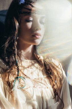 beautiful girl with braids in hairstyle posing in white boho dress on grey with lens flares  clipart