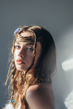 Saç stili örgülü genç, çıplak boho kız. Gri üzerinde merceklerle poz veriyor. 