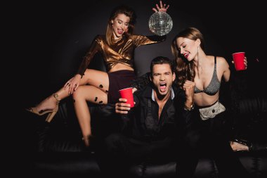 çekici ve gülümseyen arkadaşlar ellerinde disko topu ve siyah arka planda plastik bardaklar 