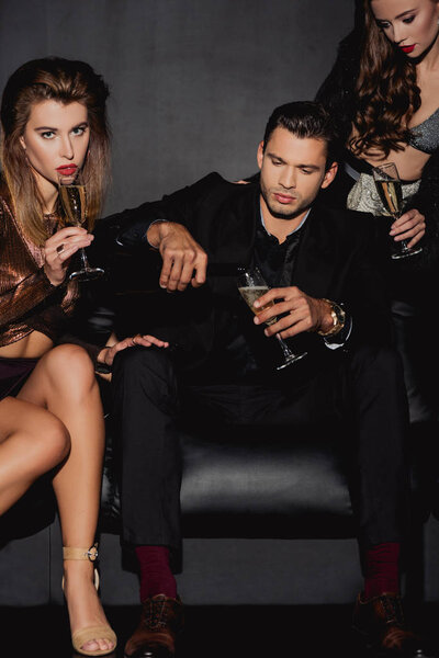 handsome man  pouring champagne for attractive and stylish women isolated on black