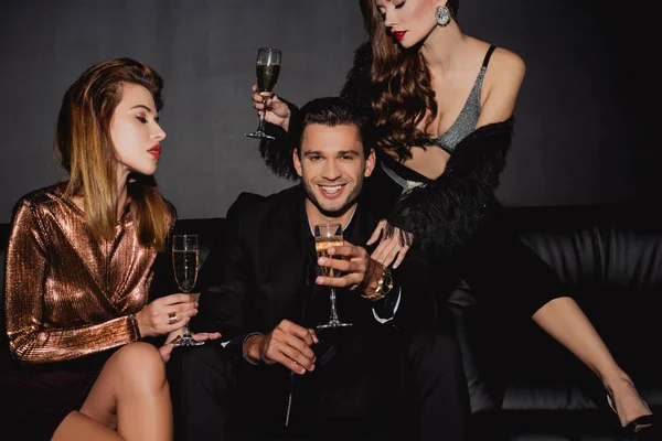 Çekici kadınlar ve elinde şampanya bardakları olan gülümseyen bir adam.