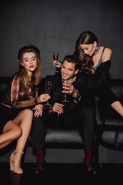 attractive women and smiling man holding champagne glasses isolated on black