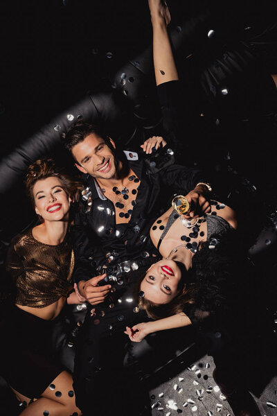 top view of attractive and smiling women and handsome man with champagne glass on black background 