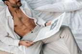 cropped vie of bi-racial man holding newspaper with business lettering in morning 