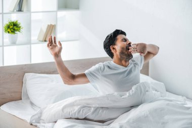 Yakışıklı, çift ırklı bir adam sabah esniyor ve uyanıyor. 