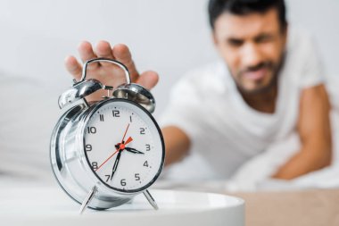 selective focus of bi-racial man holding alarm clock in morning  clipart