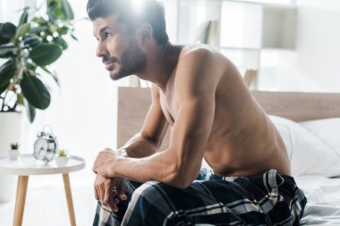 Sabahları yatakta oturan yakışıklı ve seksi çift ırklı adamın yan görüntüsü. 