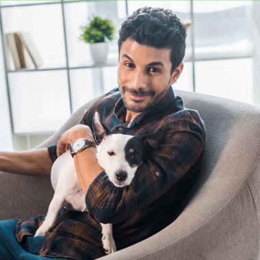 Gülümseyen ve yakışıklı çift ırklı adam Jack Russell Terrier 'ı tutuyor.