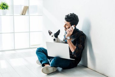 Akıllı telefondan konuşan ve Jack Russell Terrier 'ı tutan iki ırklı yakışıklı bir adam.