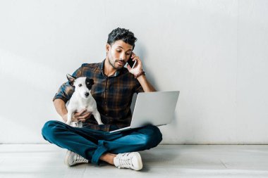 Akıllı telefondan konuşan ve Jack Russell Terrier 'ı tutan iki ırklı yakışıklı bir adam.