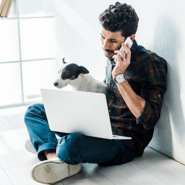 Akıllı telefondan konuşan ve Jack Russell Terrier 'ı tutan iki ırklı yakışıklı bir adam.