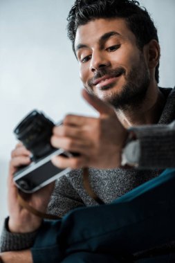 Dijital kamera tutan yakışıklı ve gülümseyen iki ırklı adamın düşük açılı görüntüsü