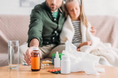 selective focus of father taking cough syrup while sitting near diseased daughter clipart