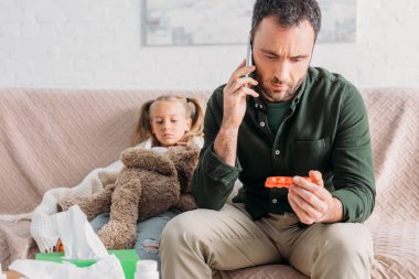 Ciddi bir adam elinde haplarla telefonuyla konuşuyor. 