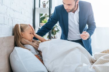 Endişeli baba termometreyi hasta kızın yanında tutuyor.