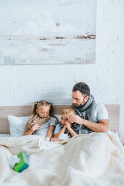 diseased man and children in warm scarfs lying in bed under blanket clipart