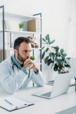 Düşünceli doktor dizüstü bilgisayarın yanında otururken gözlerini kaçırıyor.