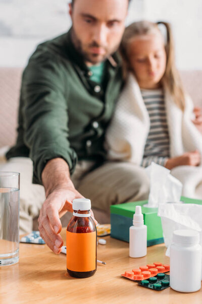 selective focus of man taking cough syrup while sitting near diseased daughter