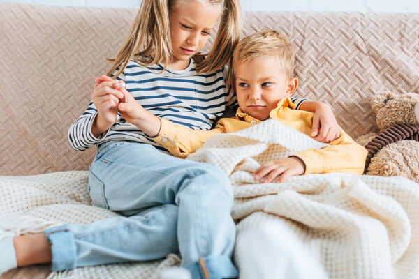 attentive sister holding pill near sick, displeased brother