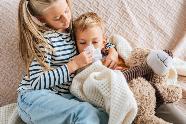 caring sister wiping nose of sick brother with napkin
