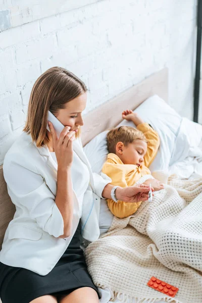 Besorgte Mutter Schaut Auf Thermometer Und Telefoniert Auf Smartphone Während — Stockfoto