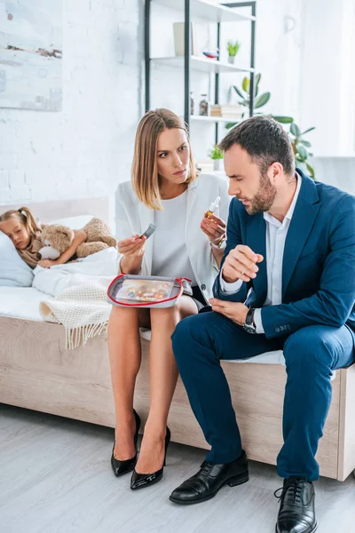 Besorgte Eltern Offizieller Kleidung Sitzen Mit Verbandskasten Auf Sofa Neben — Stockfoto