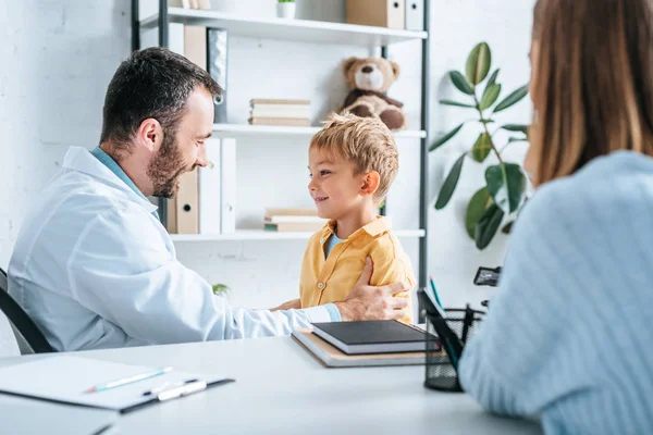 Pediatra Positivo Examinando Niño Sonriente Cerca Madre Sentado Escritorio — Foto de Stock