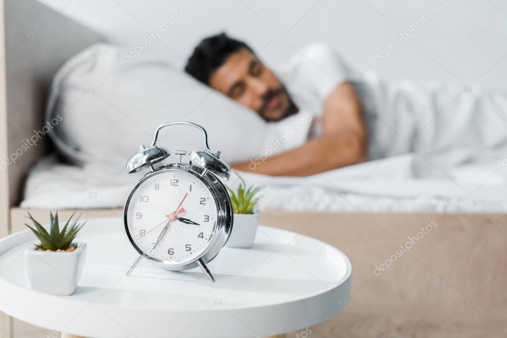 selective focus of alarm clock, plants and handsome bi-racial man sleeping on background 