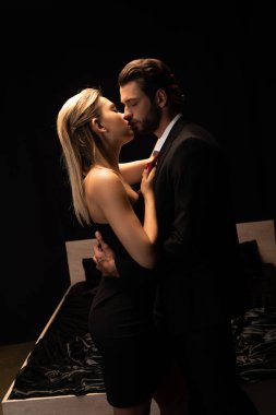 Güzel, seksi çift karanlık odada yatağın yanında öpüşüyor.