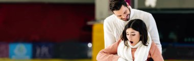 panoramic shot of handsome smiling man catching scared falling woman on skating rink clipart