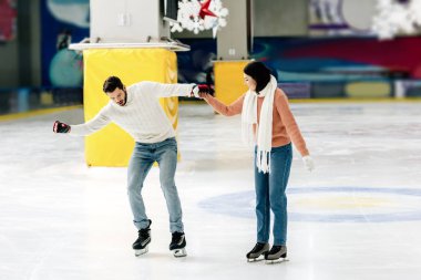 beautiful young woman teaching man to skate on a rink and holding hands clipart