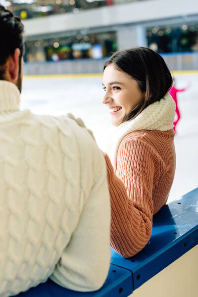 young smiling couple in sweaters spending time on skating rink  