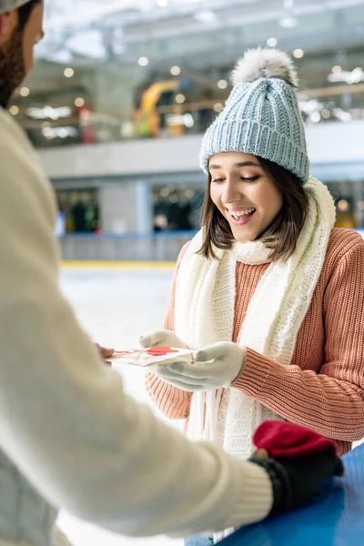 スケートリンクの幸せな女性にバレンタインデーにグリーティングカードを与える男 — ストック写真