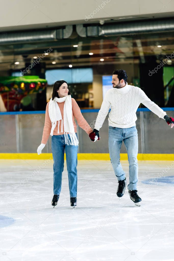 beautiful young couple in sweaters skating on rink 
