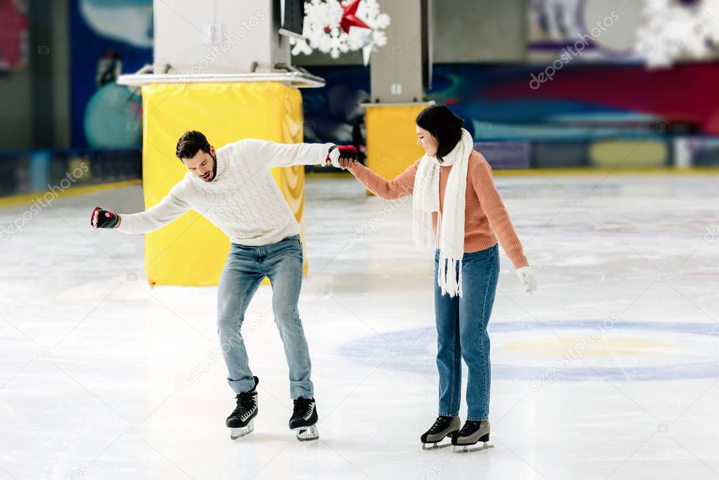 beautiful young woman teaching man to skate on a rink and holding hands