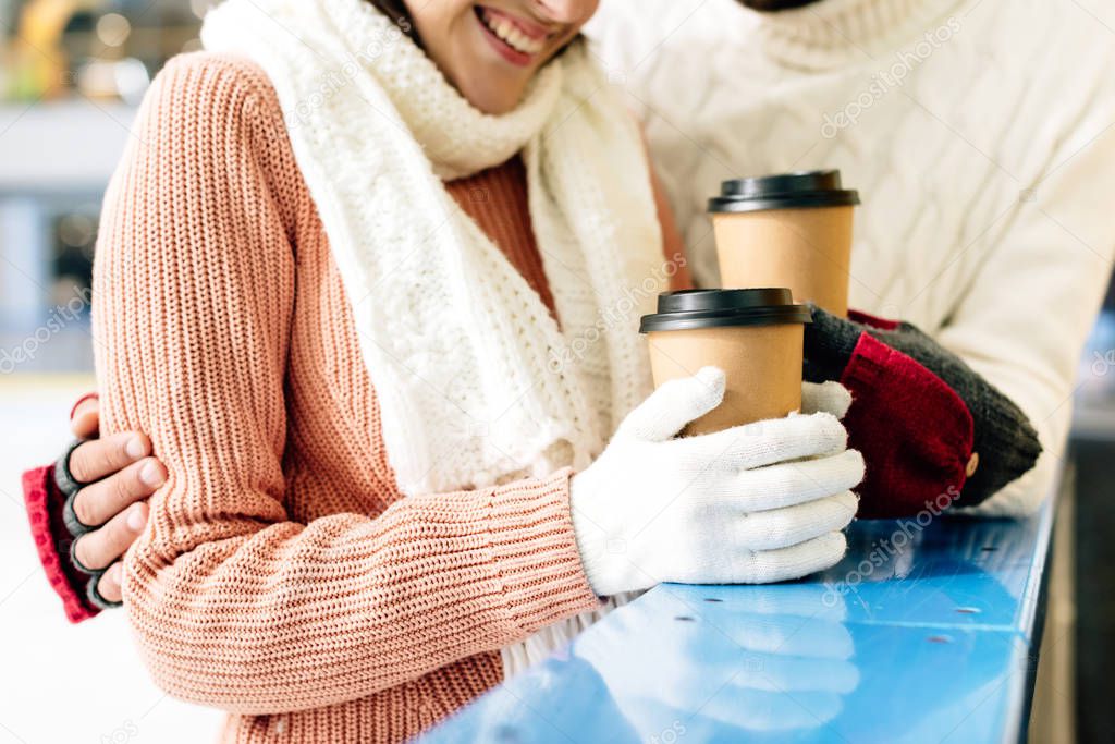 cropped view of happy couple holding coffee to go on skating rink